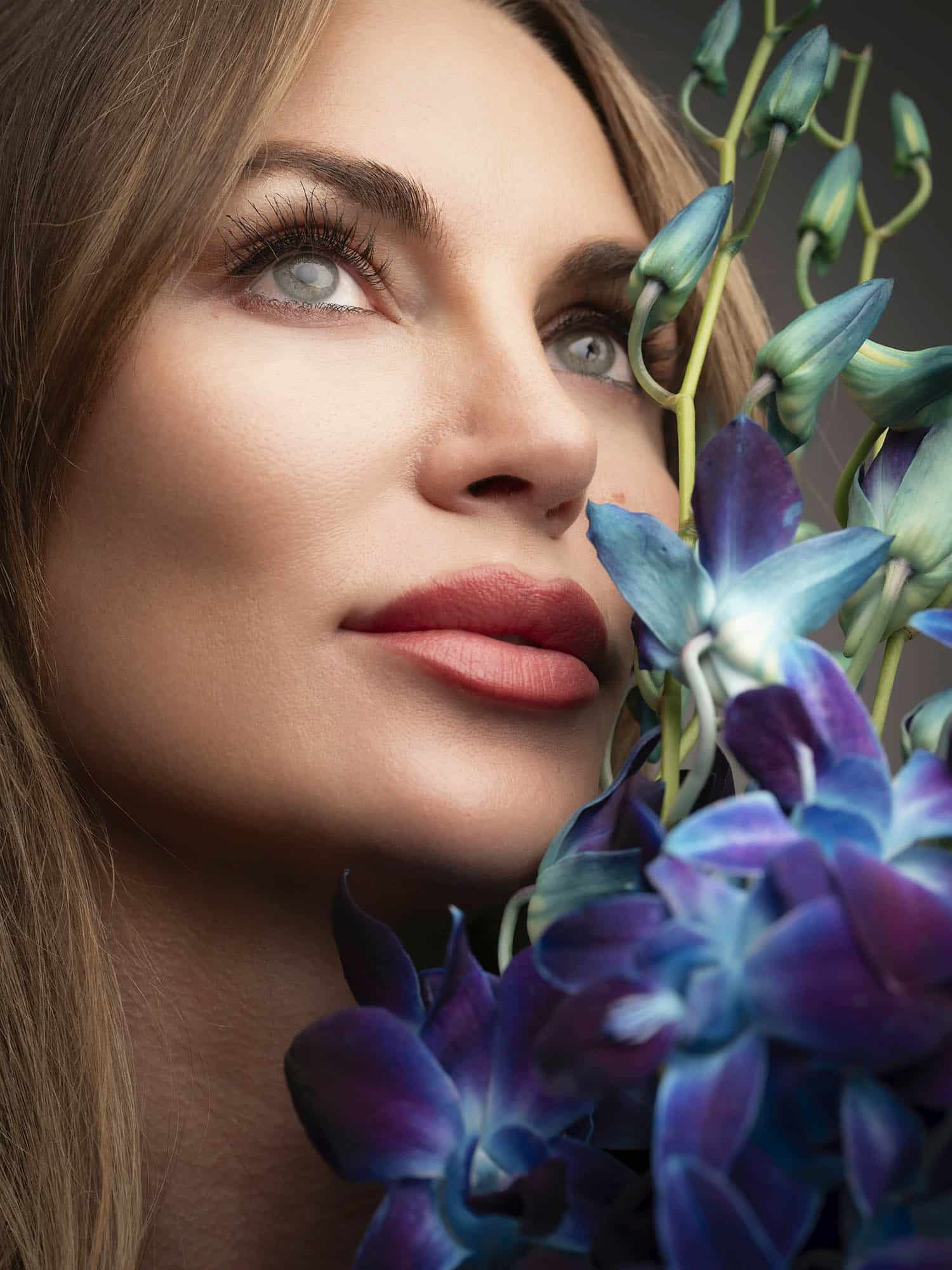 Close-up of woman with radiant skin and orchid flowers, representing rejuvenation treatments